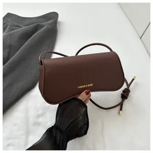 Detail of dark brown crocodile pattern underarm bag with gold logo and thin strap
