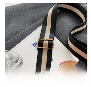 Detail of adjustable black and white striped nylon bag strap with gold metal buckle