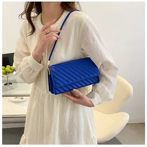 Detail of bright blue quilted shoulder bag with gold hardware worn on white dress