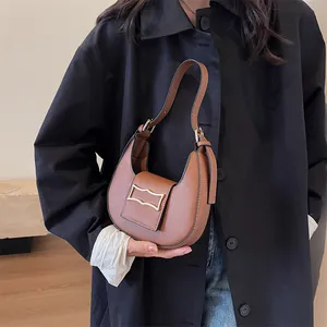 Sac bandoulière demi-lune en cuir marron mat avec boucle dorée porté sur un manteau noir