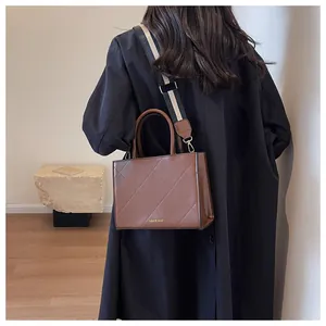 Detail of brown quilted square handbag with wide woven strap and fashion branding