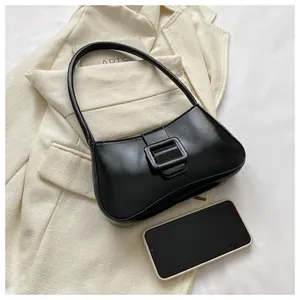 Close-up of black PU leather shoulder bag with buckle detail next to a smartphone