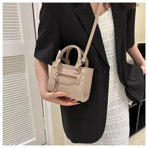 Detail der beigefarbenen Handtasche mit Krokodilmuster, dekorativen Zippern und Quasten