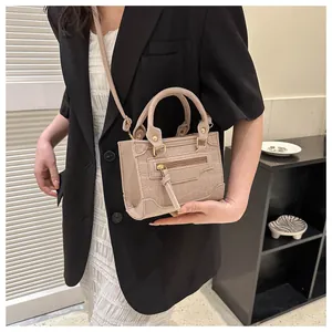 Detail der hellbeigen Handtasche mit Krokodilmuster, Goldbeschlägen und Quasten-Deko