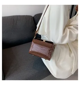Dettaglio di una borsa a tracolla marrone a trama coccodrillo con fibbie dorate su modella