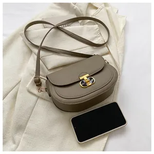 Detail of taupe saddle bag with golden clasp next to a phone for size scale comparison