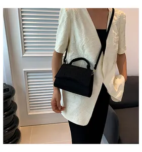 Detail shot of a black crocodile pattern felt handbag worn with a beige textured blazer