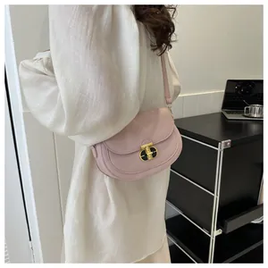 Detailed view of a pink saddle bag featuring a gold metal twist lock and lychee leather texture