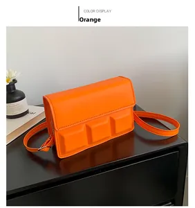 Detail van helder oranje crossbodytas met moderne geometrische reliëfklep op display
