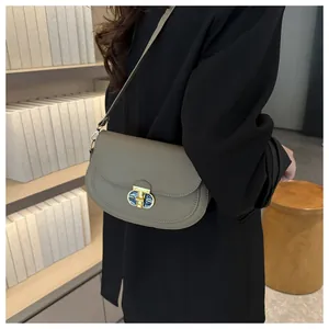 Detail of taupe saddle bag featuring a gold lock with blue enamel and pebble grain texture