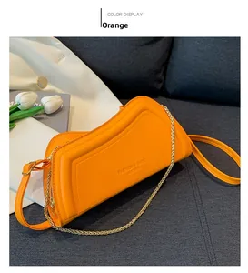 Detailansicht der orangefarbenen Leder-Baguette-Tasche mit Logo auf grauem Kissen