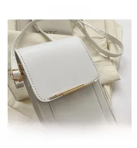 Detailed view of white leather mini crossbody bag featuring a gold metal bar and buckle strap