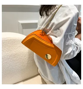 Detail der leuchtend orangen asymmetrischen Umhängetasche mit goldener Schnalle und Kette