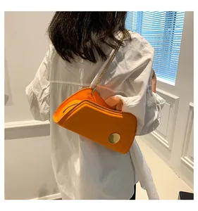 Detailansicht der leuchtend orangefarbenen asymmetrischen Ledertasche mit Goldkette
