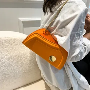 Leuchtend orangefarbene asymmetrische Achseltasche mit Goldkette an einem Model