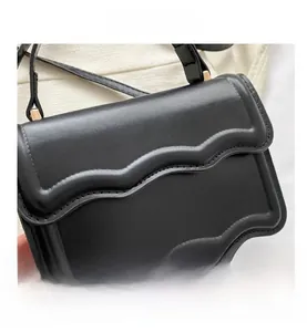 Detail shot of black crossbody bag featuring unique wavy edges and gold metal hardware