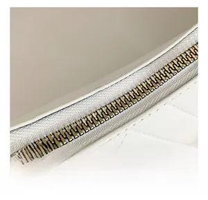 Close-up of smooth golden metal zipper on high-gloss white patent leather shoulder bag
