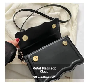 Detail of wave-edge flap and dual gold magnetic buckles on the matte black leather bag