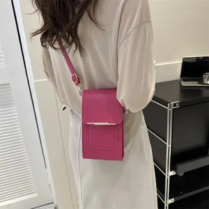 Magenta leather crossbody phone bag with gold metal trim shown on a model in a room