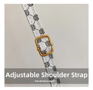 Detail of adjustable white leather shoulder strap with clover pattern and gold metal buckle
