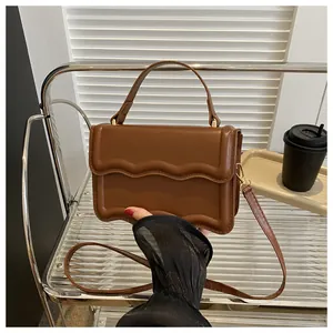 Caramel square bag with wavy edge flap and gold hardware on minimalist metal shelf