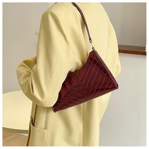 Detail of burgundy patent leather underarm bag with V-shaped quilting and asymmetric design
