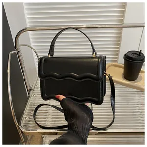Detailed view of black matte leather handbag with scalloped flap and gold hardware