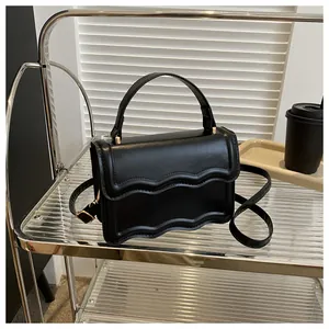 Detail view of the elegant wavy edge design and gold hardware on this black crossbody bag
