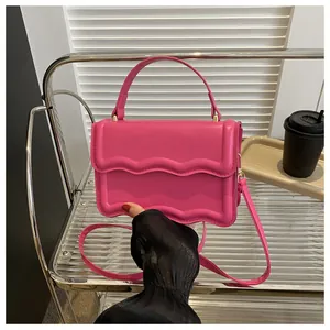 Detail of rose red crossbody bag with wavy edge design and gold hardware on glass table