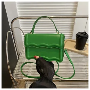 Close-up of green square handbag with wavy edge flap on a metal cart