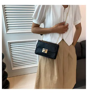 Detail of black faux crocodile pattern bag with gold chain strap and metal clasp