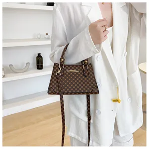 Close-up of a brown patterned crossbody bag with gold hardware and a white blazer outfit