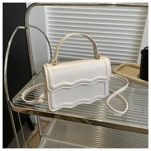 Detail of cream square bag with wavy flap edge and gold hardware on glass shelf