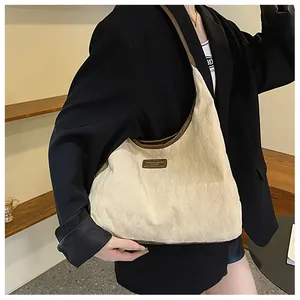 Détail d'un sac cabas crème matelassé avec bordure brune et écusson cuir sur mannequin