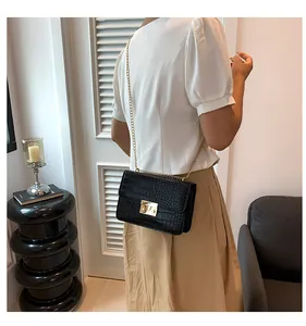 Detail of a black faux-crocodile leather bag with gold buckle on a crossbody chain strap