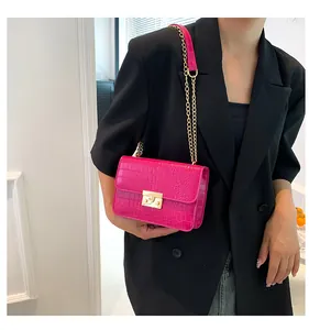 Detail of hot pink crocodile pattern crossbody bag with gold chain strap on black suit