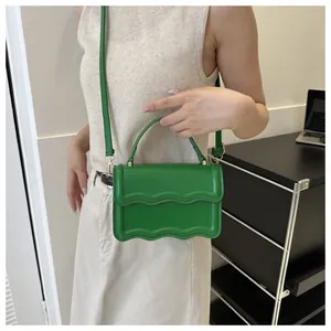 Detail of a bright green crossbody bag with unique wavy edges and golden hardware