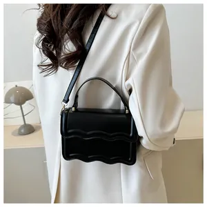 Detail of minimalist black square bag with wave-edge flap design and leather texture