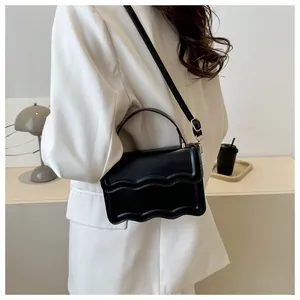 Detail of black leather crossbody bag featuring wave-edge flap and gold metal clasp hardware