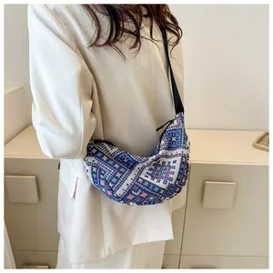 Detail of a crescent-shaped crossbody bag with blue and beige ethnic woven texture