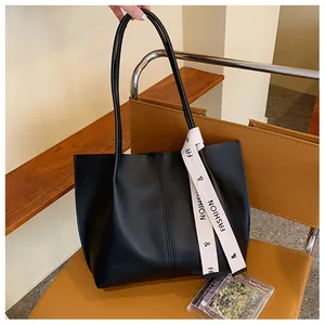 Detail of black tote bag with matte texture and contrast letter print ribbon on a brown chair