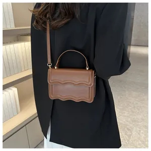 Detail view of brown faux leather crossbody bag with unique wavy flap and gold hardware
