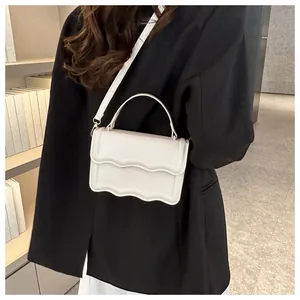 Close-up of a white minimalist handbag with wavy edges worn over a black blazer
