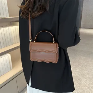 Brown scallop edge crossbody square bag shown with a model in a warm library setting