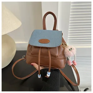 Close-up of mini denim and leather backpack with FAUTOR logo and pink plush charm