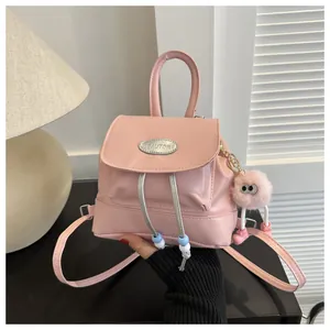 Close-up of a pink faux leather mini backpack with a metal logo and plush ball charm