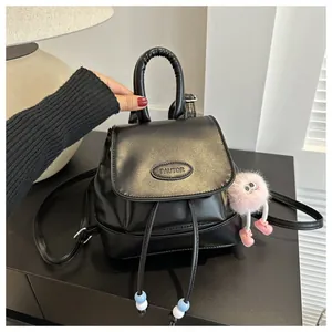 Detail of a mini black leather backpack with drawstring closure and pink plush charm