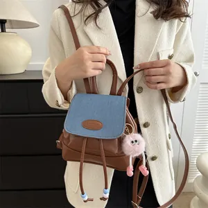 Vintage denim and brown leather mini backpack with plush doll keychain on a model