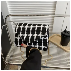 Detalle de bolso bandolera de tweed con cadena dorada en estante de acrílico