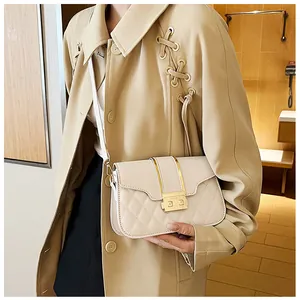 Detail of a minimalist beige quilted crossbody bag with golden metal clasp on a coat